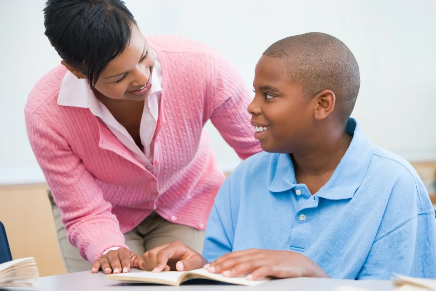 A teacher leaning in to help a student read from a book