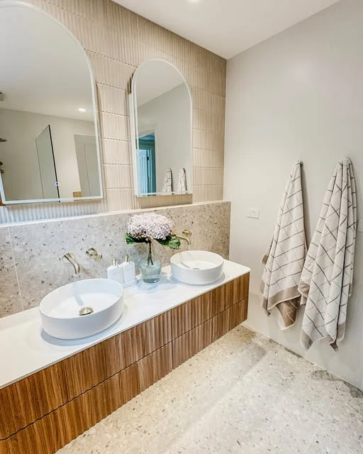 Double vanity bathroom with arched mirrors and a terrazzo floor, tiled by Greyscale Tiling