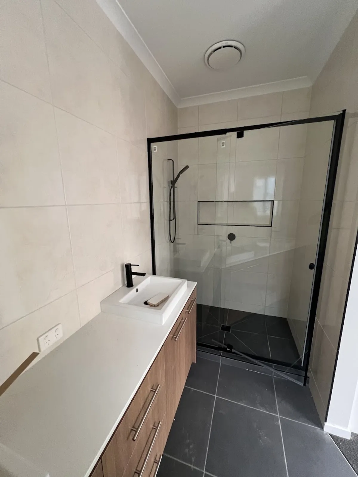 A finished ensuite by Tiles and Baths Solutions, stone look walls, black framed shower and charcoal floor