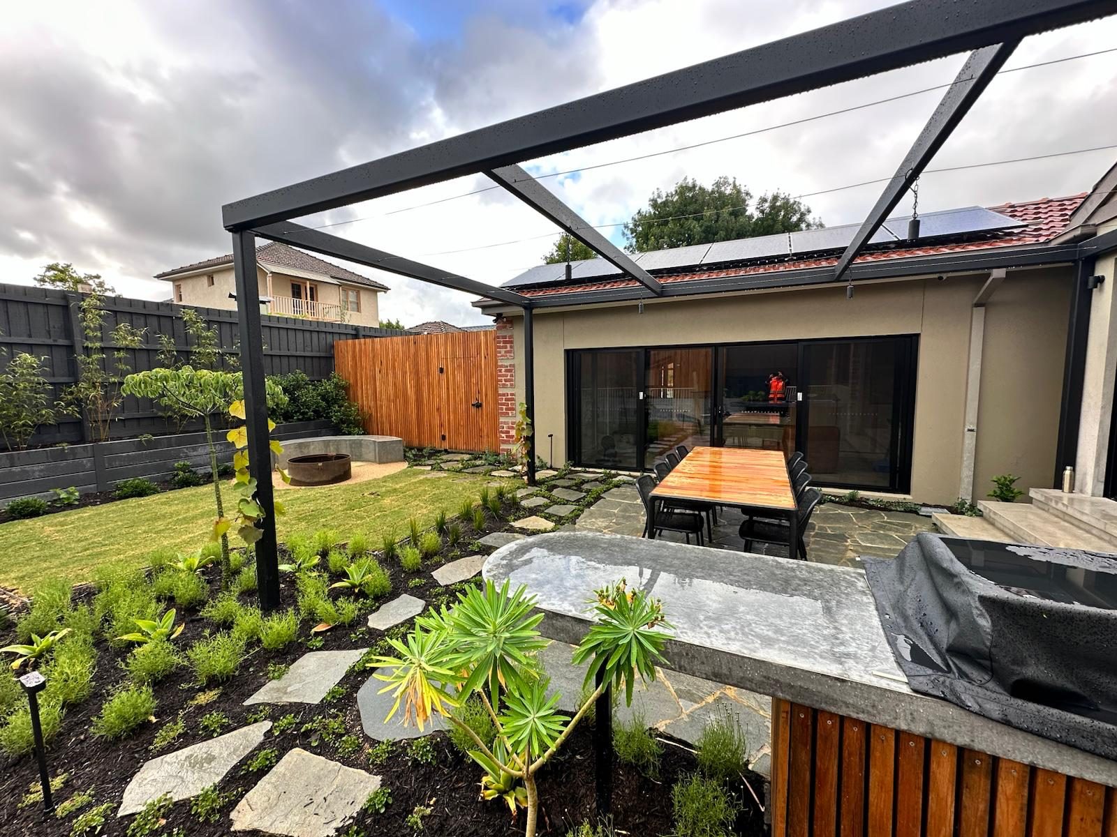 New backyard landscape with steel pergola, stepping stones, fresh planting and outdoor dining