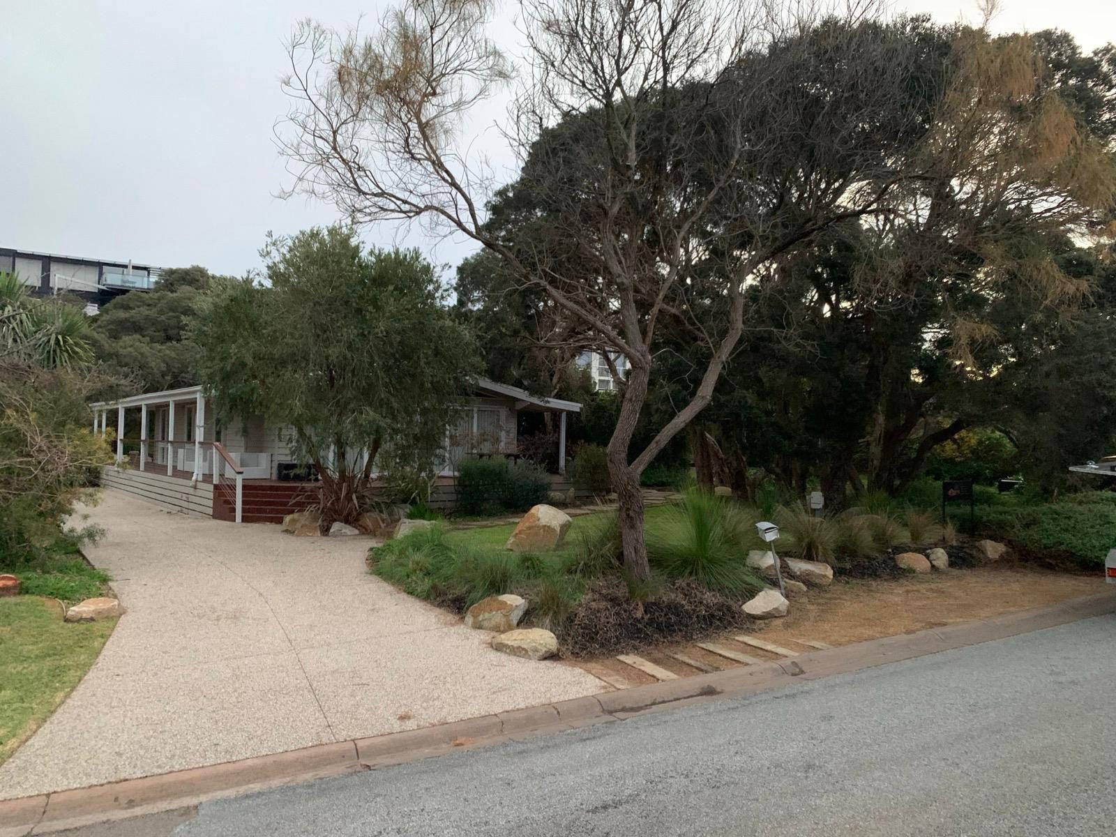 Coastal home frontage with boulder garden beds and exposed aggregate driveway
