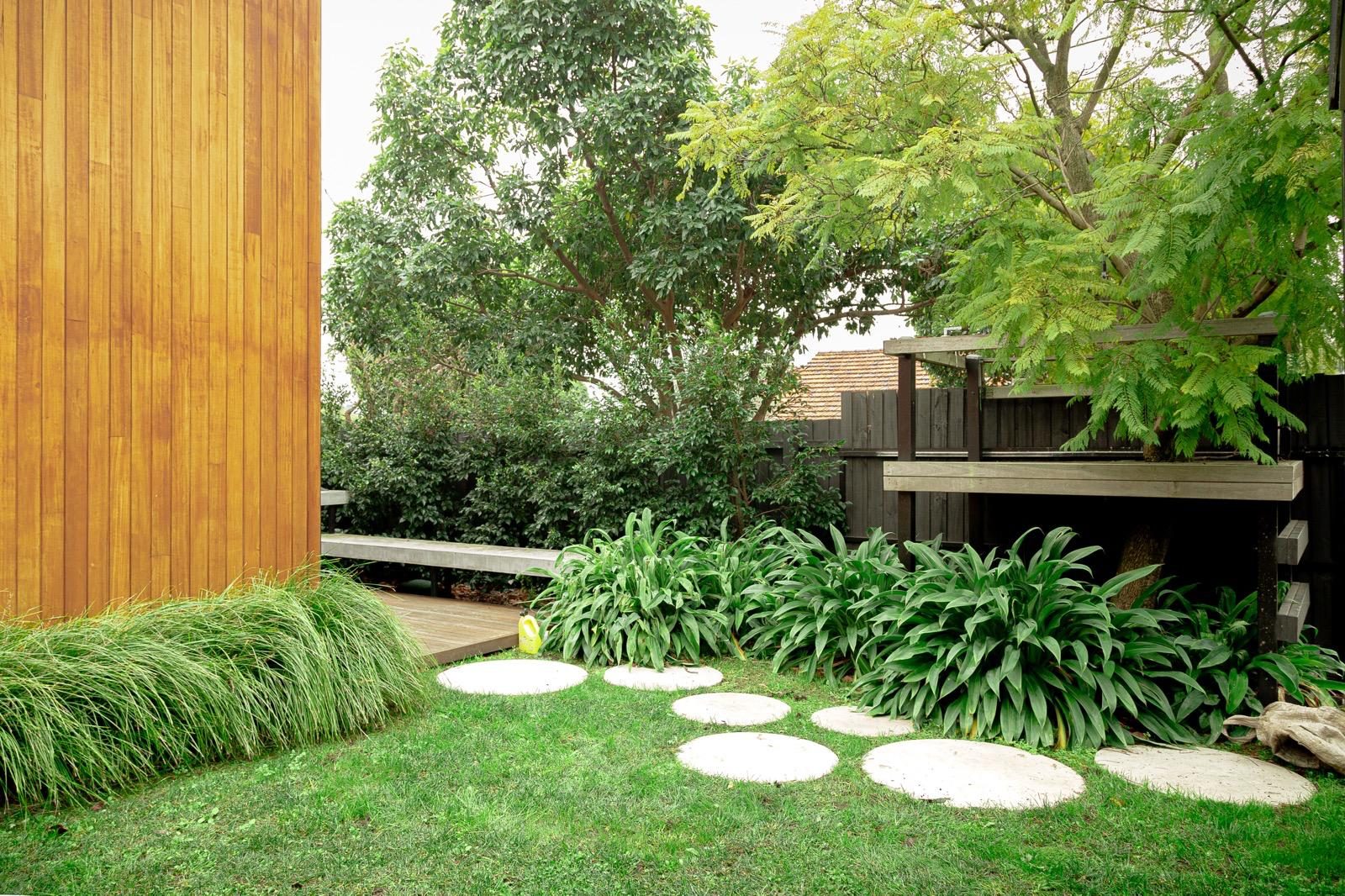 Round stepping stones across a lawn with lush green garden beds