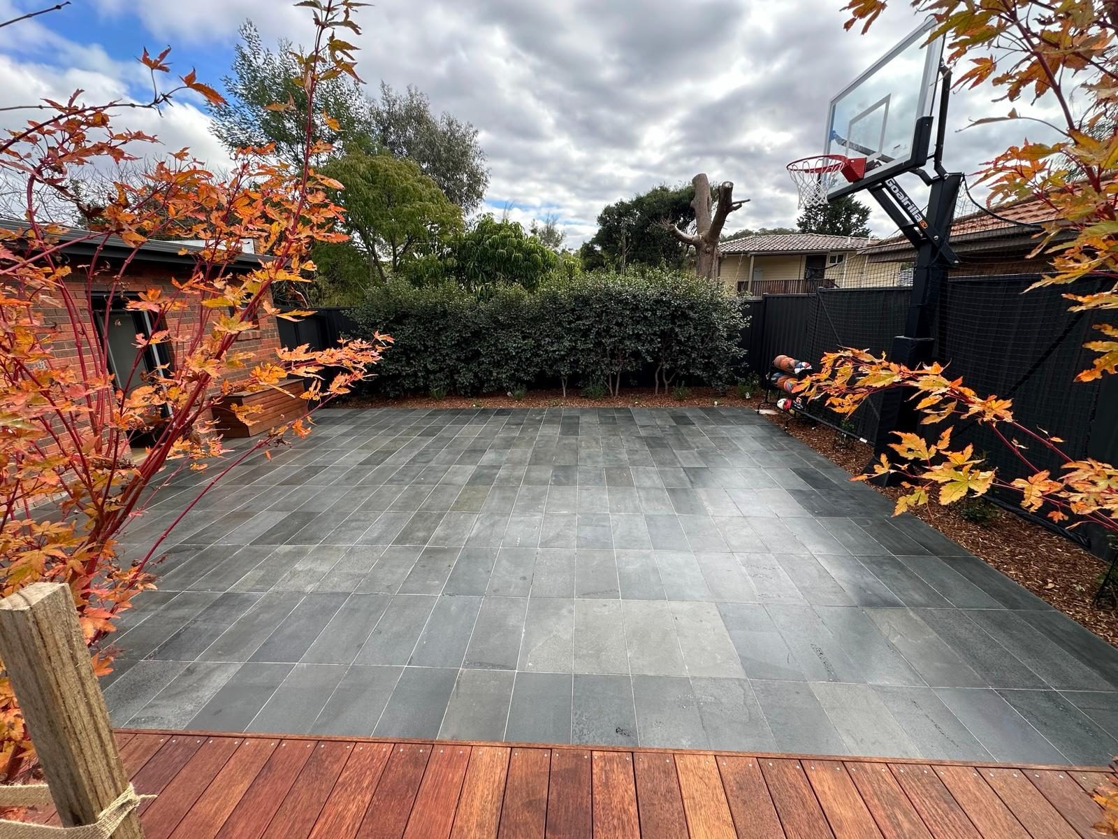Slate-paved court with timber deck edging framed by autumn maples