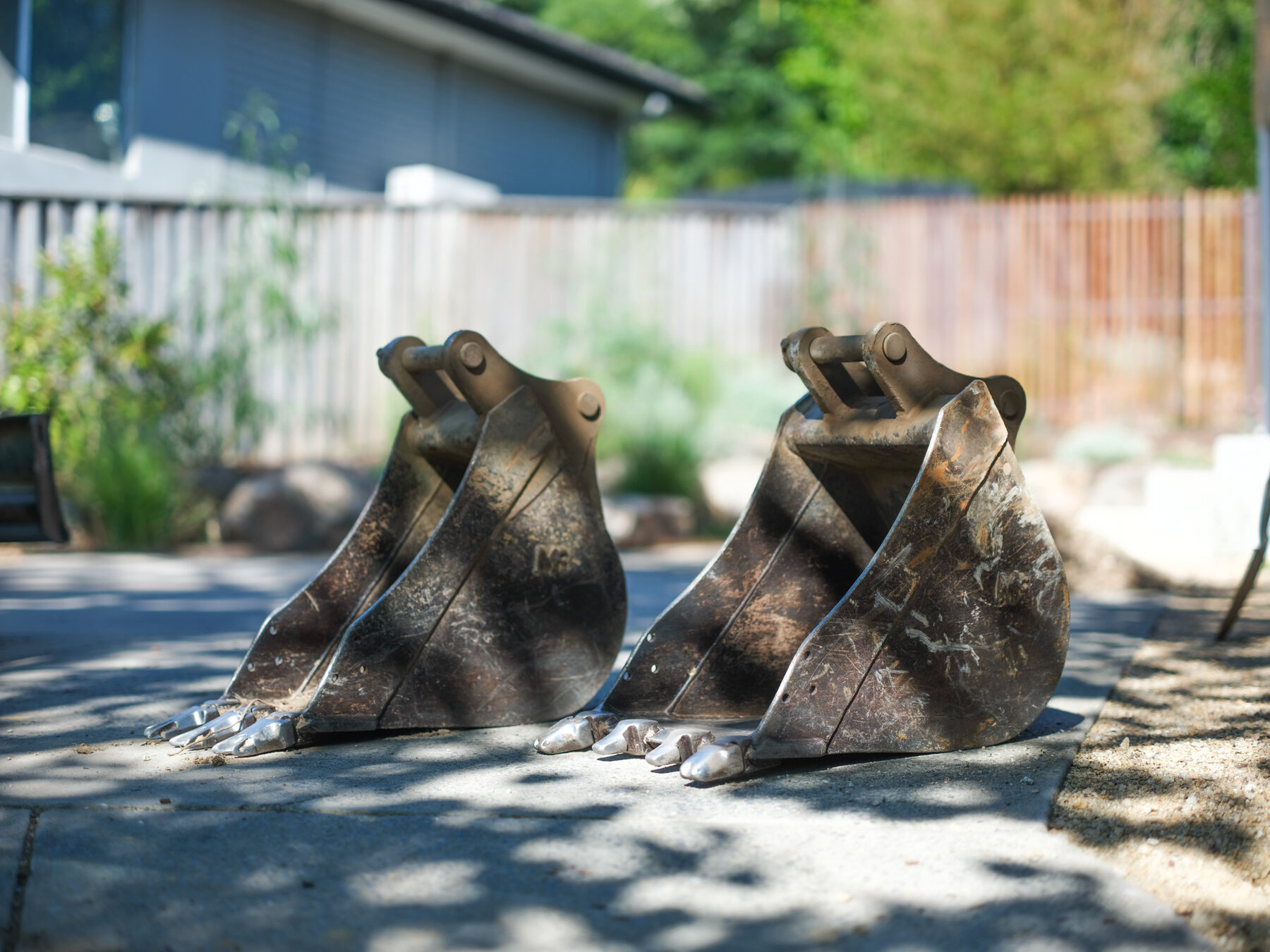 Two excavator buckets sitting on a driveway on site