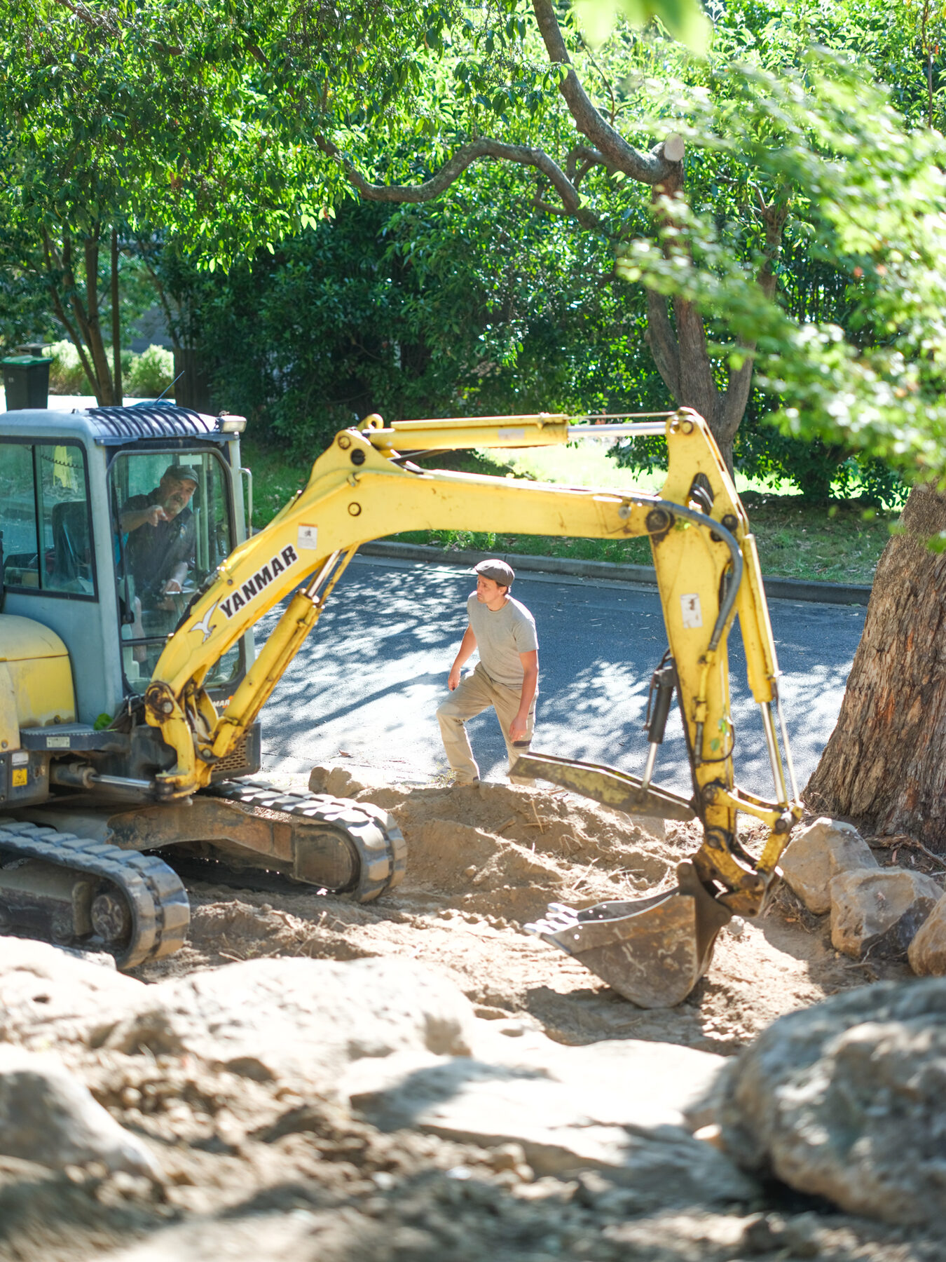 Excavator lowering a rock into place with a landscaper guiding it
