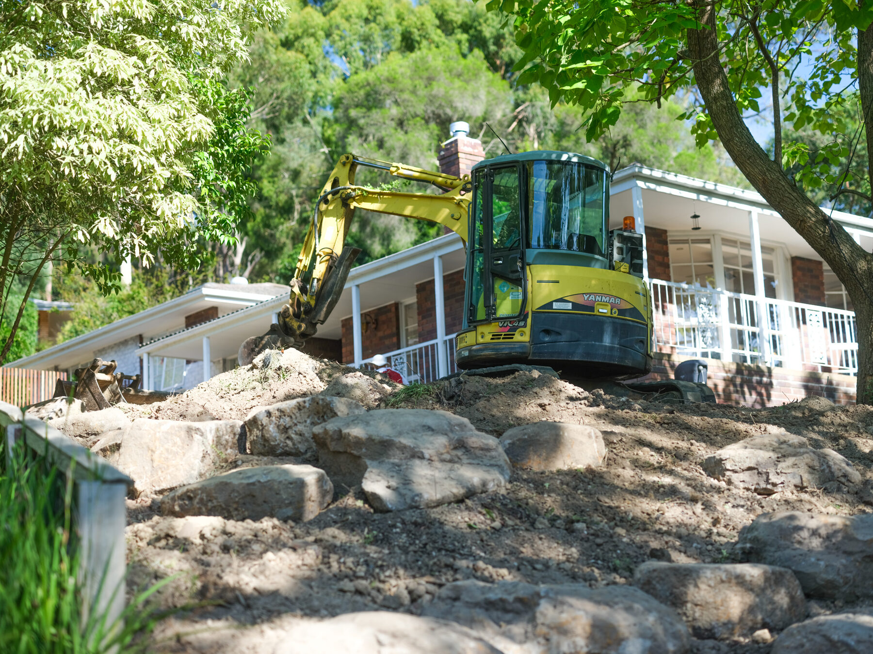 Excavator setting boulders for a rock wall in a front garden