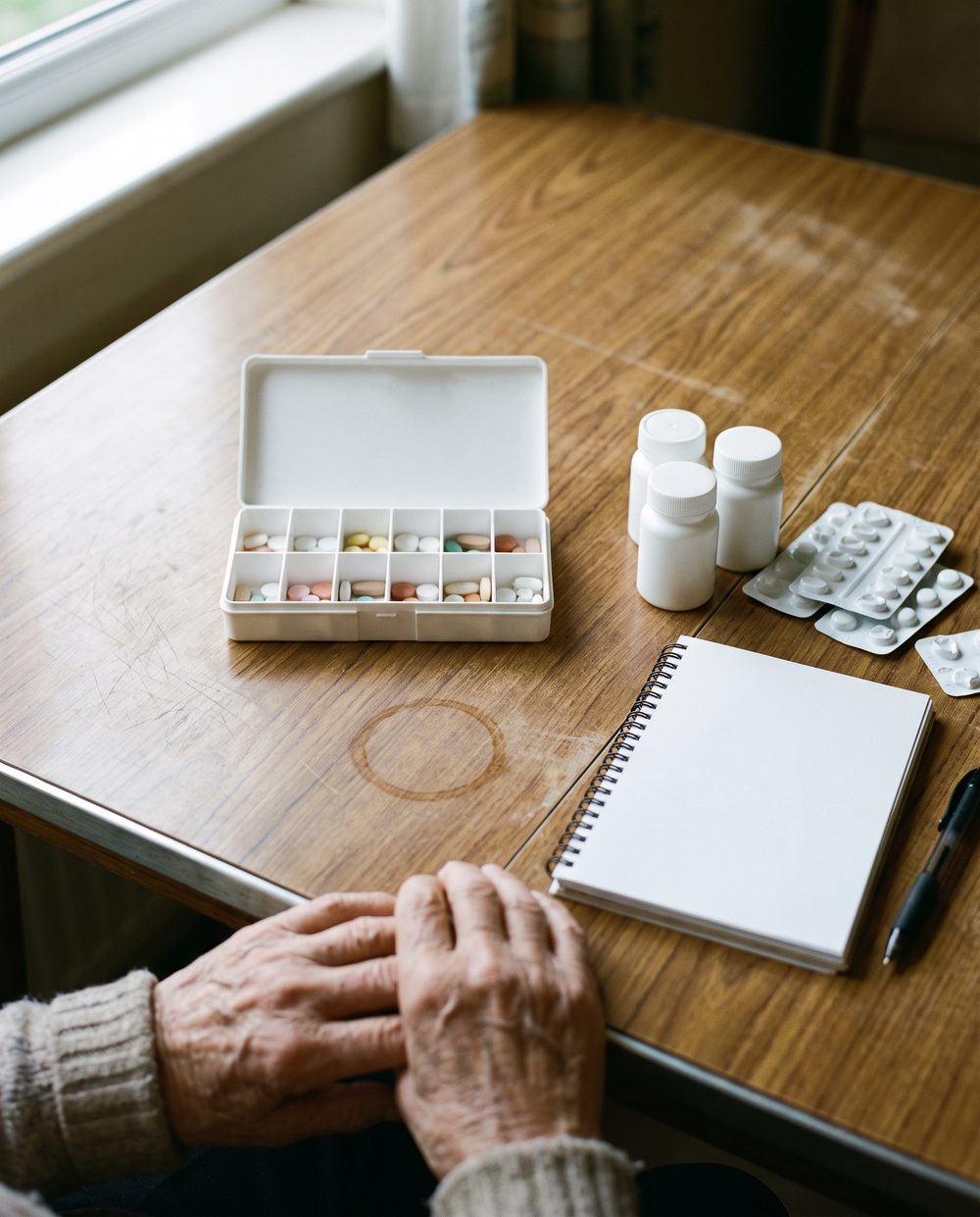 A weekly pill organiser, tablets and a notebook laid out on a kitchen table at a home visit