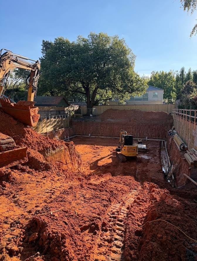 A deep excavation in orange clay with a mature tree left standing