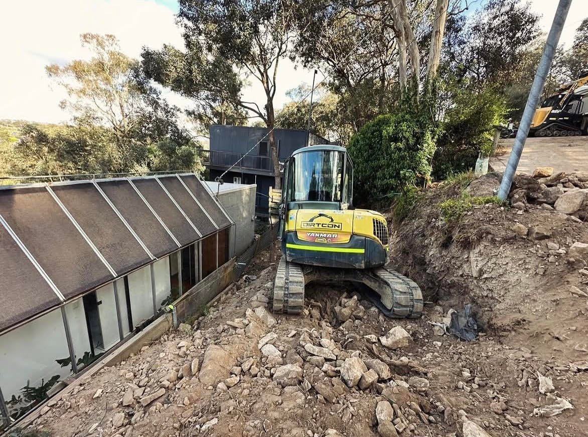 An excavator working close beside a house on rocky ground