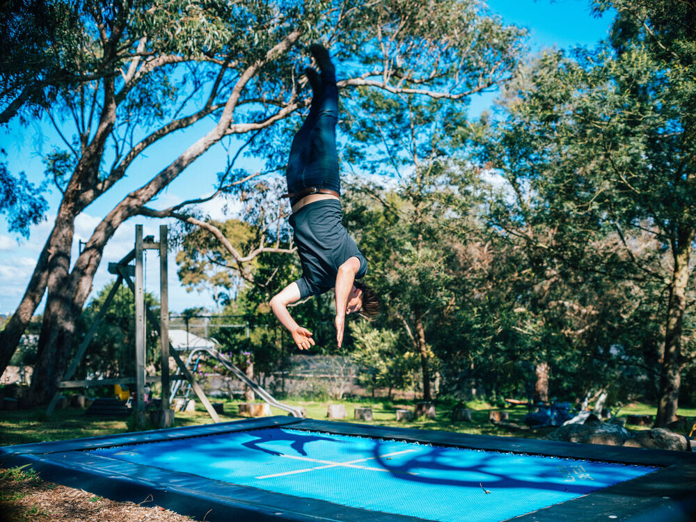 Ollie mid backflip above the trampoline with gum trees behind him