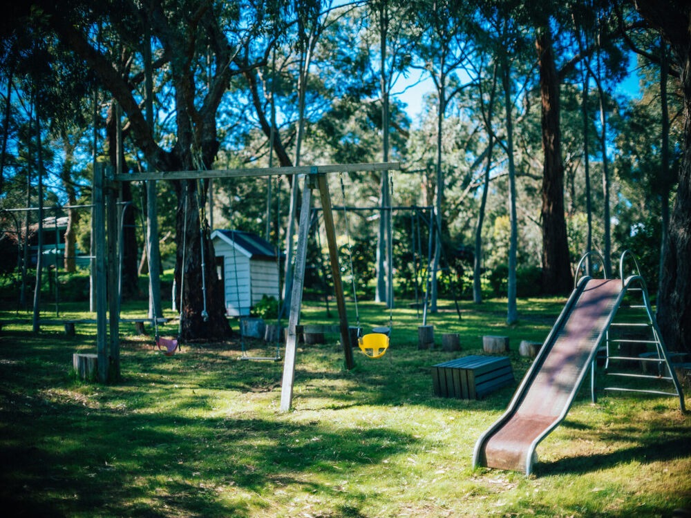 A wooden swing set and slide under the gum trees in the back garden