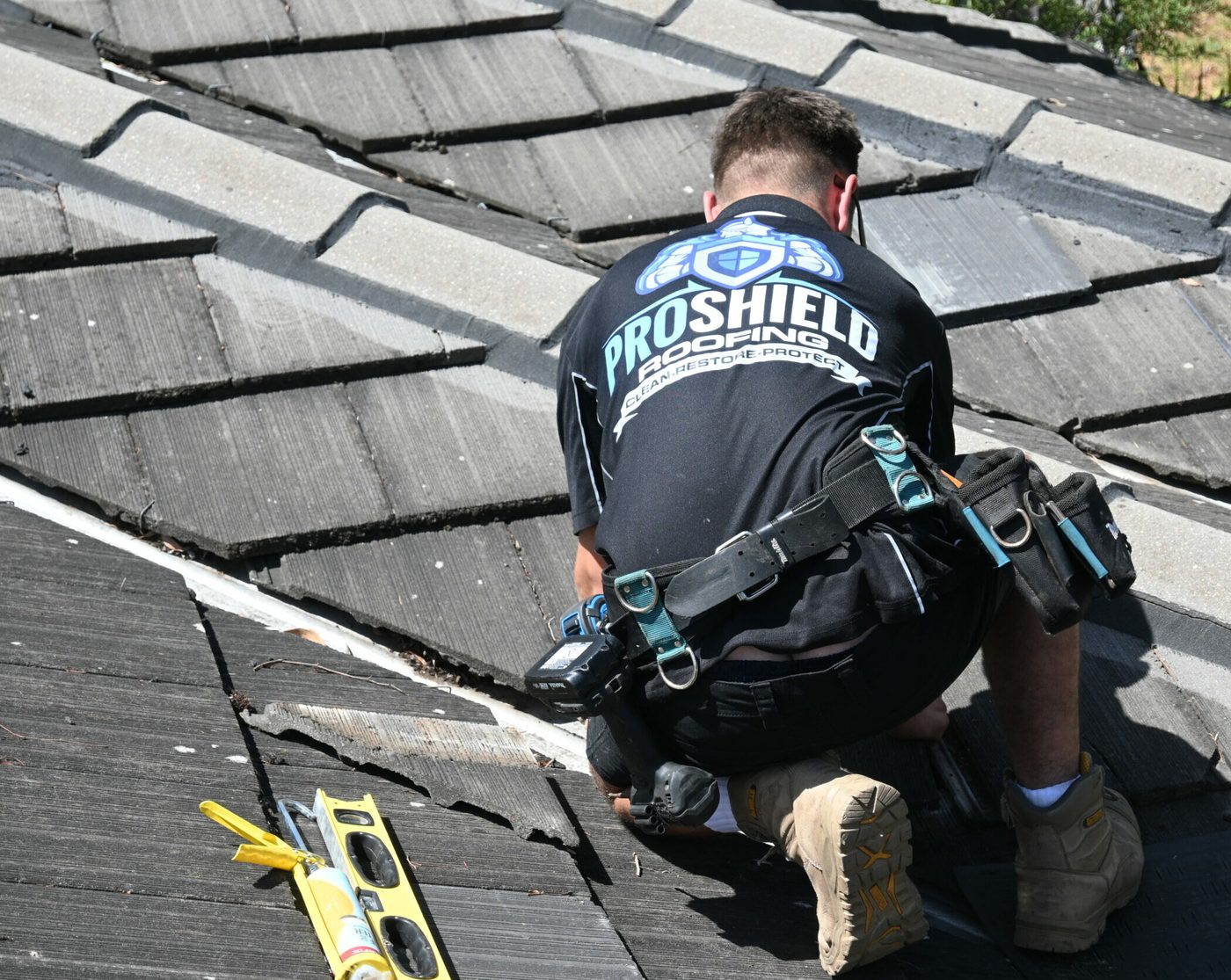 A Pro Shield roofer in a branded shirt working along a tile roof